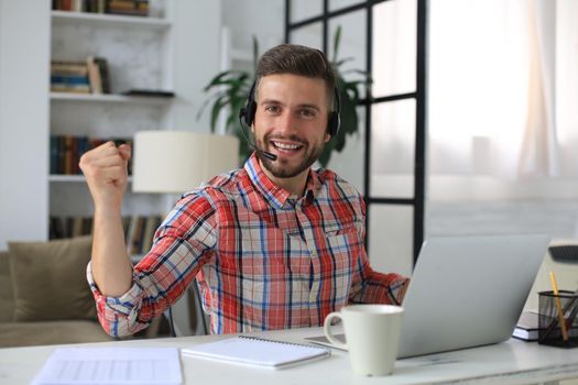 Handsome businessman is keeping arms raised and expressing joyful at home office