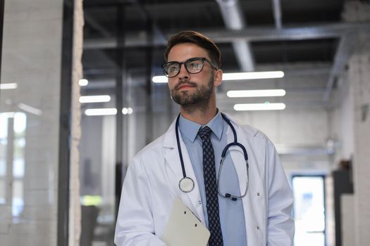 Handsome friendly young doctor on hospital corridor looking at camera, smiling