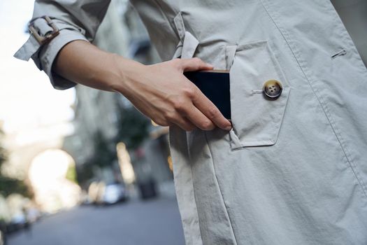 Cropped shot of a woman in grey coat putting her smartphone in pocket while standing outdoors. People lifestyle and technology concept