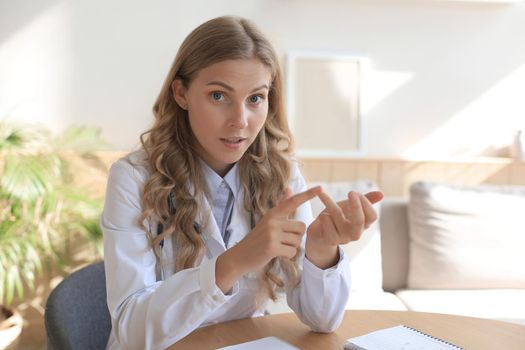 Smiling attractive female doctor talking at camera with patient