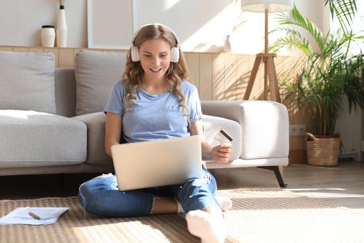 Happy natural blonde using credit card and laptop in the living room