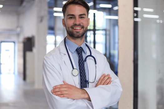 Handsome friendly young doctor on hospital corridor looking at camera, smiling
