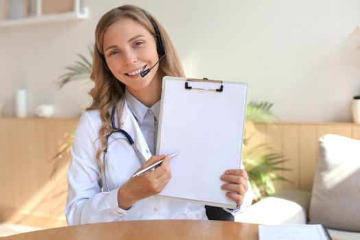 Smiling attractive female doctor talking at camera with patient