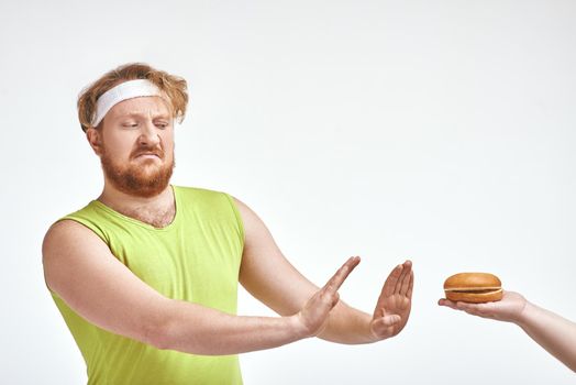 Funny picture of red haired, bearded, plump man on white background. A human giving a sandwich for man, but man doesn't want to take it