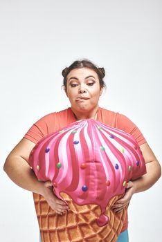 Funny picture of amusing, brunette, chubby woman on white background. Woman is holding a huge ice cream