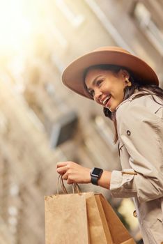Shopping makes her feel good. Vertical shot of a young excited woman wearing grey coat and hat carrying shopping bags, standing on city street and smiling. Fashion, people lifestyle