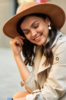 Vertical shot of a young attractive happy woman wearing hat looking aside and smiling while spending time outdoors. People lifestyle concept