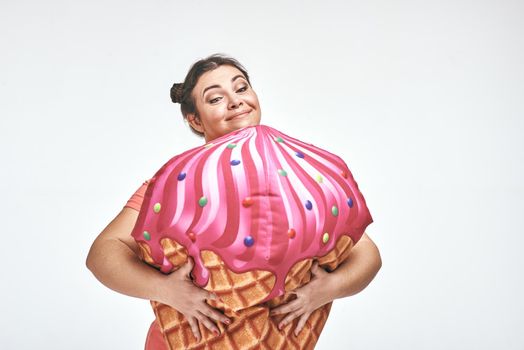 Funny picture of amusing, brunette, chubby woman on white background. Woman is holding a huge ice cream