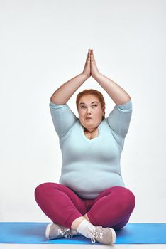 Funny picture of amusing, red haired, chubby woman on white background. Woman trains on the mat.