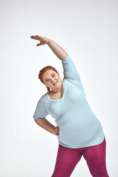 Funny picture of amusing, red haired, chubby woman on white background. Woman trains.