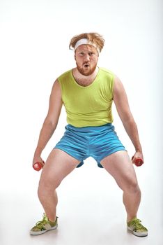 Funny picture of red haired, bearded, plump man on white background. Man wearing sportswear. Man holding the dumbbells