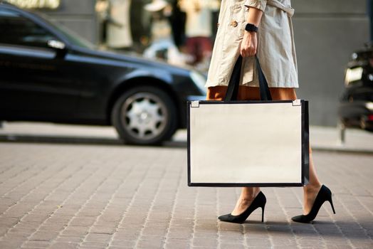 Shopping day. Cropped shot of woman wearing high heel shoes carrying big shopping bag walking city streets. Fashion, people lifestyle concept