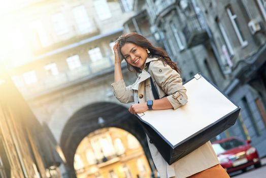 Shopping day. Young attractive and stylish woman with big shopping bag standing on city street, looking at camera and smiling. Fashion, people lifestyle concept