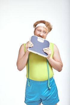 Funny picture of red haired, bearded, plump man on white background. Man holding the scales