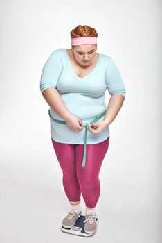 Picture of chubby woman on white background. Woman is measuring her belly