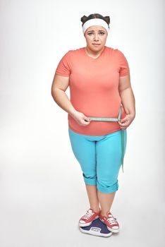 Picture of chubby woman on white background. Woman is measuring her belly