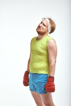 Funny picture of red haired, bearded, plump man on white background. Man wearing sportswear and red boxing gloves