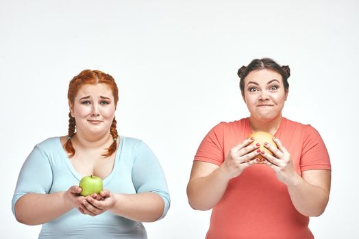 Funny picture of amusing chubby women on white background. One woman holding a sandwich, the other holding an apple.