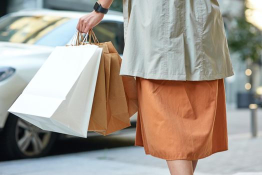 Rear view of a woman carrying shopping bags while walking city streets, cropped shot. People lifestyle concept