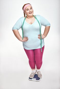 Funny picture of amusing, red haired, chubby woman on white background. Woman is smiling while standing on scales