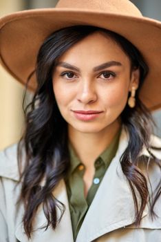 Close up portrait of a young attractive caucasian woman wearing hat looking at camera while standing outdoors. Fashion, beautiful people concept