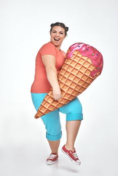 Funny picture of amusing, brunette, chubby woman on white background. Woman is holding a huge ice cream