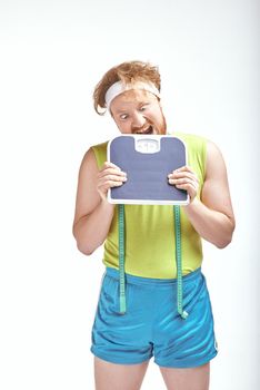 Funny picture of red haired, bearded, plump man on white background. Man holding the scales
