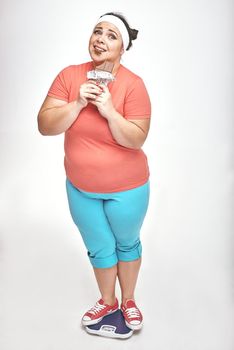 Funny picture of amusing, chubby woman on white background. She is eating chocolate while standing on the scales