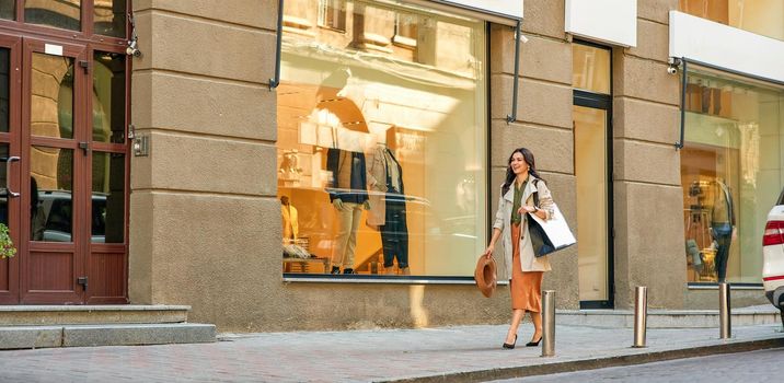 Full length of a young happy stylish woman with shopping bag walking city streets, visiting fashion boutiques or shops, panoramic banner. Fashion, people lifestyle concept