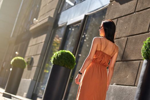 Rear view of a young attractive woman wearing long romantic dress walking city streets on a sunny day. People lifestyle and fashion concept