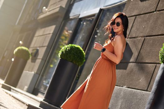 Young happy attractive woman wearing long romantic dress posing outdoors, looking at camera and smiling while walking city streets on a sunny day. People lifestyle and fashion concept