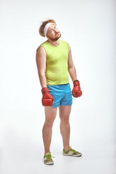 Funny picture of red haired, bearded, plump man on white background. Man wearing sportswear and red boxing gloves