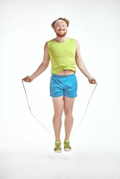 Funny picture of red haired, bearded, plump man on white background. Man wearing sportswear. Man holding skipping rope.