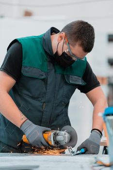 Heavy Industry Engineering Factory Interior with Industrial Worker Using Angle Grinder and Cutting a Metal Tube. Contractor in Safety Uniform and Hard Hat Manufacturing Metal Structures. High quality photo