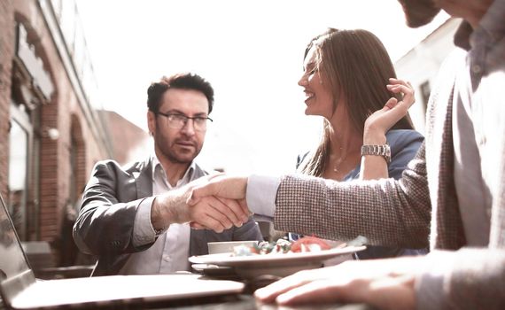 handshake colleagues at a table in a street cafe.the concept of teamwork