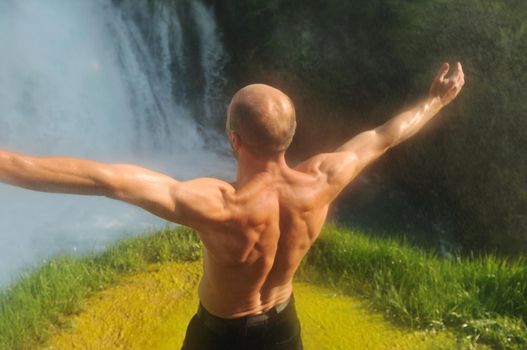 standing man with wide opened arms with waterfalls in background and representing freshness healthy lifestyle and success concept