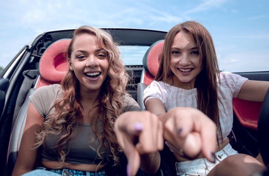 two happy girls sitting in the car and pointing at you.the concept of choice