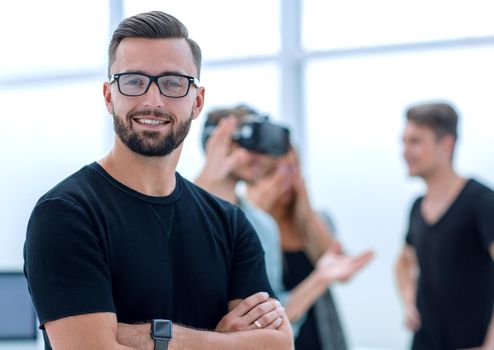 a man is standing with his hands crossed. young entrepreneurs are testing a new game in the background.