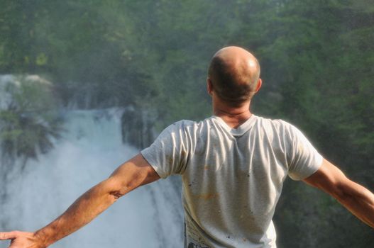 standing man with wide opened arms with waterfalls in background and representing freshness healthy lifestyle and success concept