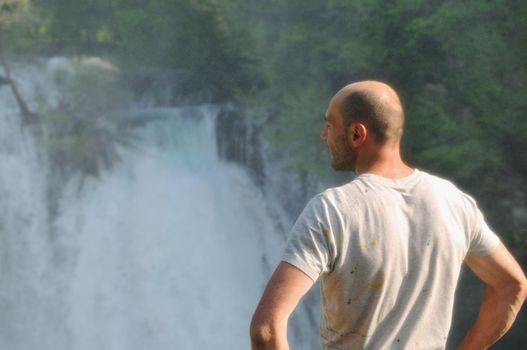 standing man with wide opened arms with waterfalls in background and representing freshness healthy lifestyle and success concept