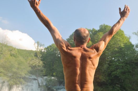 standing man with wide opened arms with waterfalls in background and representing freshness healthy lifestyle and success concept