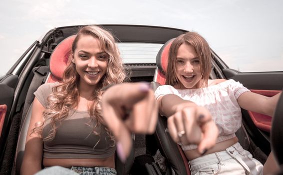 two happy young women sitting in a car and pointing at you.the concept of choice