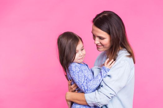 people, happiness, love, family and motherhood concept - happy little daughter hugging and kissing her mother over pink background.