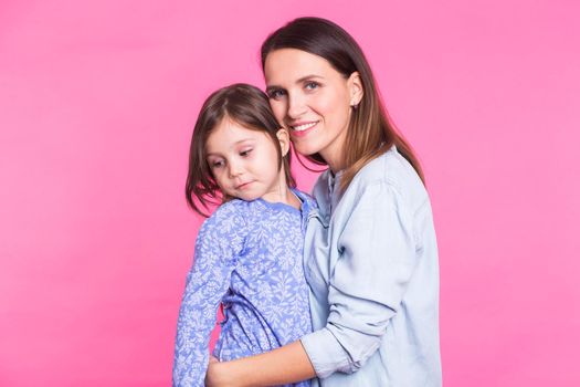 people, happiness, love, family and motherhood concept - happy little daughter hugging and kissing her mother over pink background.