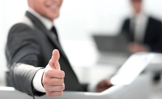 businessman on blurred background shows thumbs up while sitting in office