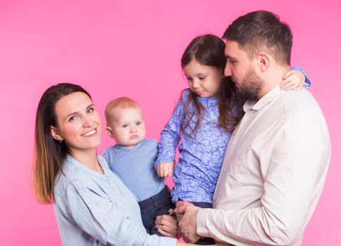 Cute family posing and smiling at camera together on pink background.