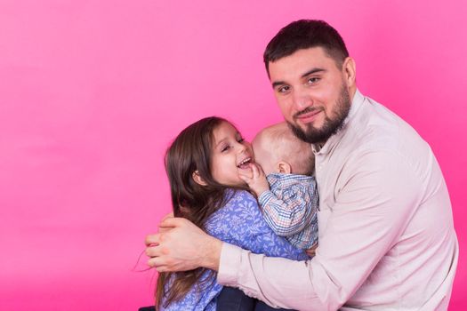 handsome father carrying his little daughter and baby son on pink background.