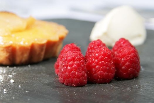 raspberries on slate bed with cream and tart in background differential focus