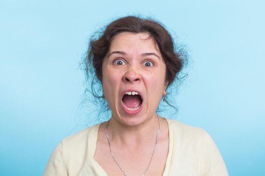 Angry aggressive woman with ferocious expression on blue background.