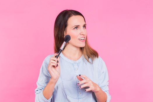 Beautiful young woman applying cosmetic powder on her face with tassel, skin care concept.